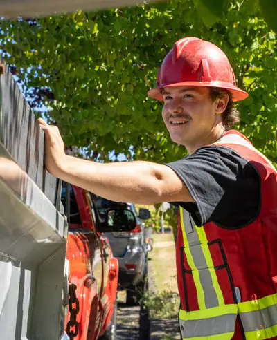 A Modern Drainage crew member in a hard hat and safety vest checking a gutter and downspout run against the fascia of a North Vancouver house.
